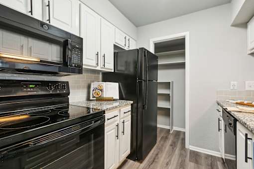 A black stove and refrigerator in a kitchen with white cabinets.