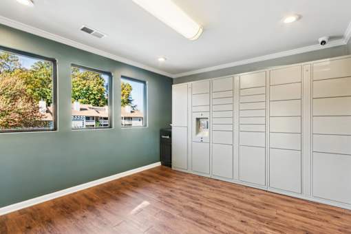 A room with wooden floors and a large window with a view of trees and houses outside.