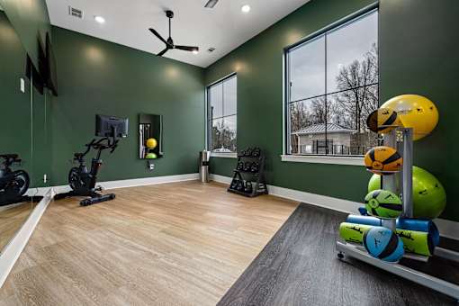 A room with a green wall and a wooden floor has exercise equipment and a television.