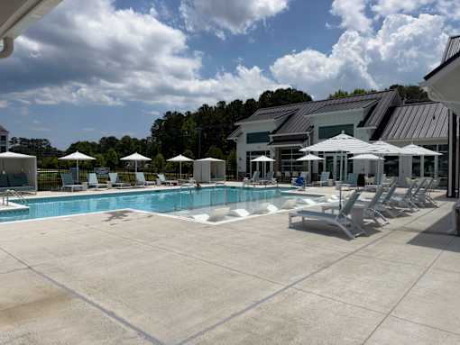 1-Bedroom Luxury Apartments In Myrtle Beach, SC - Anchor Pointe - A Large Outdoor Community Pool With White In-Pool Loungers, Private Cabanas, And Striped Sun Umbrellas.