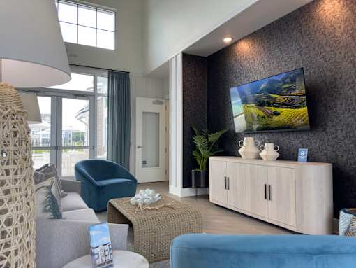 Myrtle Beach, SC, Luxury Apartments With In-Unit Washer and Dryer - Anchor Pointe - Living Room With Blue Armchairs, Coffee Table, Wall-Mounted Television, Media Console, and Glass Doors.