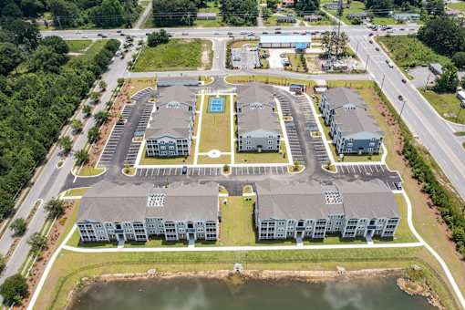 An aerial view of a large building complex with a parking lot and a body of water in front.