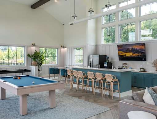 A pool table is in the middle of a room with a bar and a television.