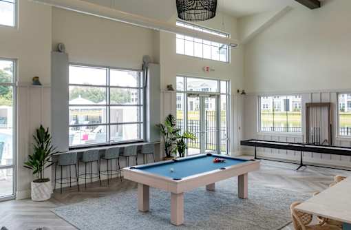 A pool table is in the middle of a room with a view of the outside.