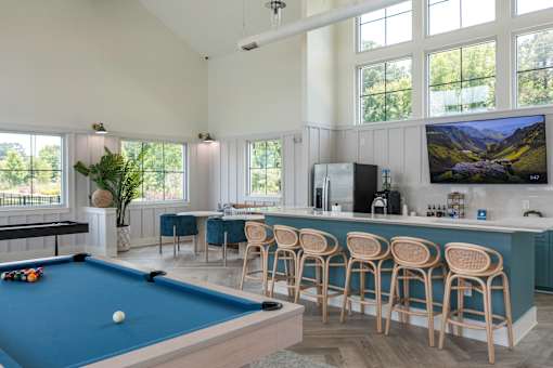A pool table is in the middle of a room with a bar and a television.