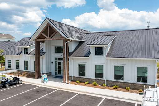 A white building with a black roof and a parking lot in front.