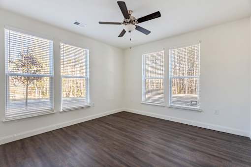 A room with a ceiling fan and three windows.