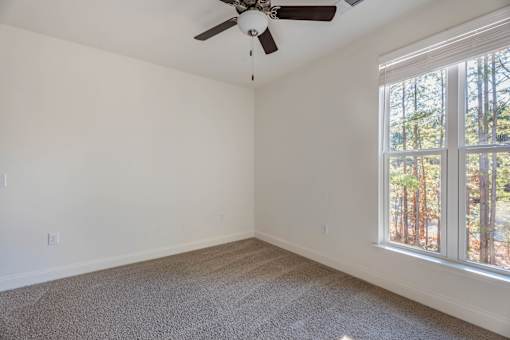 A room with a ceiling fan and a window overlooking a wooded area.