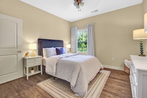 A bedroom with a bed, nightstand, and a window with curtains.