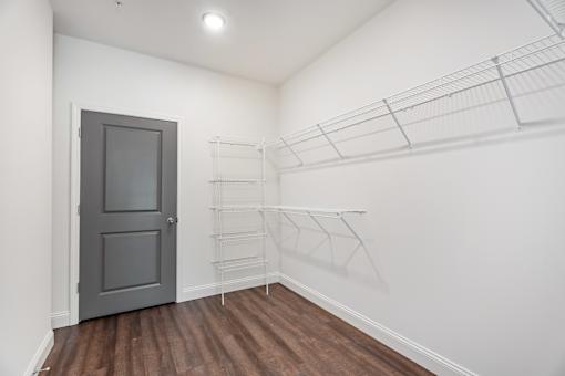 A room with a grey door and a white wall with a shelf on the wall.