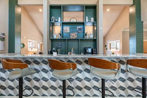 Four bar stools are in front of a bar with a green shelf behind them.