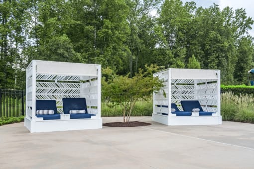 two white structures with blue chairs and a tree