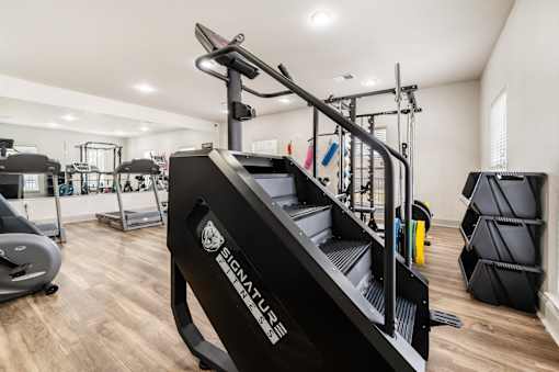 A black treadmill with the brand name SIGNATURE on it is in the foreground of a well-equipped gym.
