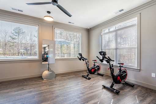 A room with a fan, exercise bikes, and a large window.