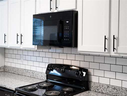 A black microwave is mounted above a black stove in a kitchen.