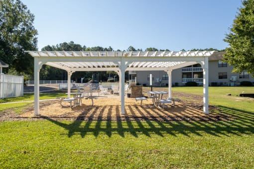 a white pergola with benches and tables in a park