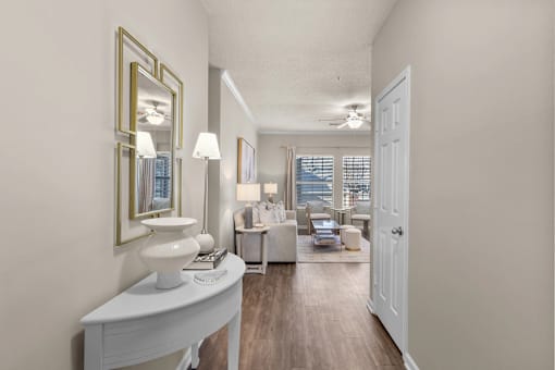 A well-lit, spacious living room with a white sofa set and a large mirror on the wall at Heights at New Garden apartments in Greensboro, NC.