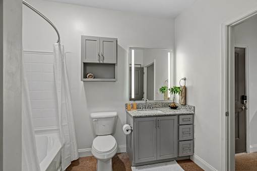 A bathroom with a white toilet, a sink with a mirror above it, and a shower with a white curtain.