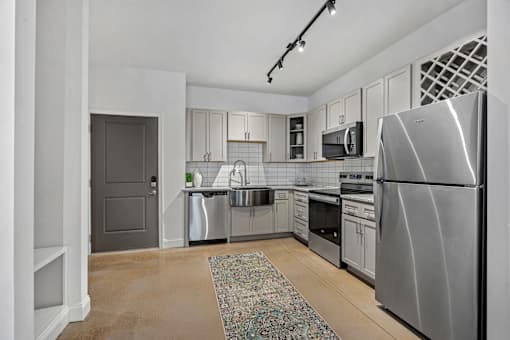 A modern kitchen with stainless steel appliances and a rug on the floor.