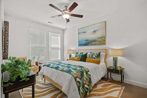 A bedroom with a bed, a ceiling fan, and a painting on the wall.
