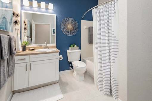 A bathroom with blue walls, a single sink, bathtub and toilet.