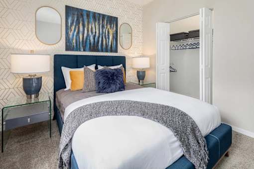A bedroom with a large bed, nightstands with lamps and a closet door open.