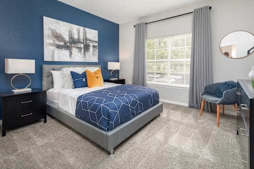A bedroom with a large bed, a chair, a nightstand, and a large window with curtains.