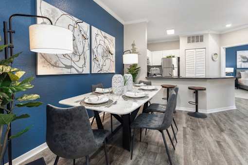 A dining room with a table set and a kitchen area in the background.