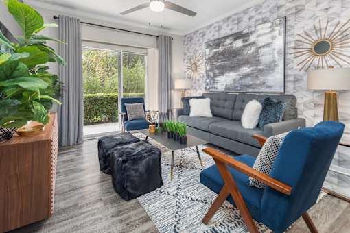A living room with a grey couch, a blue chair, tv, and large window with curtains.