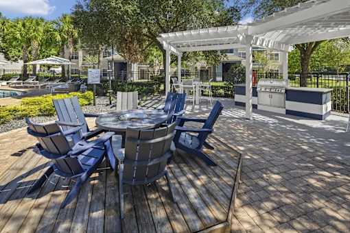 Outdoor wooden deck with blue chairs in a circle and a white pergola in the background.