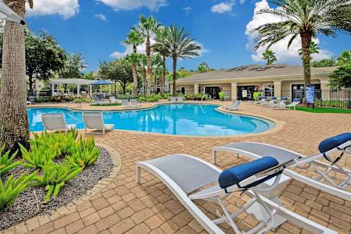 Outdoor pool surrounded by palm trees and lounge chairs.