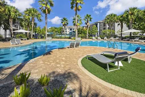 A swimming pool surrounded by palm trees and lounge chairs with a circle of green grass.