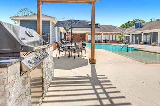 A patio with a grill and a pool in the background.
