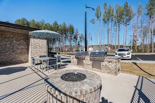 A patio with a fire pit and chairs under a blue umbrella.