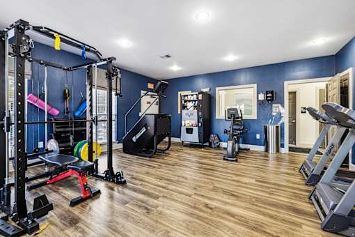 A gym with a variety of equipment including a squat rack, bench, and treadmill at Evergreen at the Bluffs apartments in Knoxville, TN.