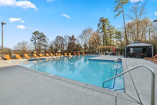 A large outdoor swimming pool with orange lounge chairs and a small building to the right at Evergreen at the Bluffs apartments in Knoxville, TN..