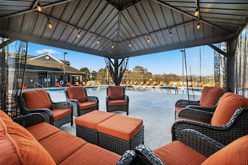 A patio with orange cushioned chairs and tables under a roof at Evergreen at the Bluffs apartments in Knoxville, TN..