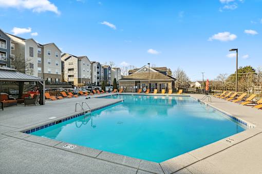 A large swimming pool surrounded by lounge chairs and apartment buildings at Evergreen at the Bluffs apartments in Knoxville, TN..