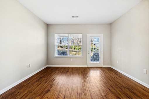 A room with wooden floors and a window showing a view of a building at Evergreen at the Bluffs apartments in Knoxville, TN.
