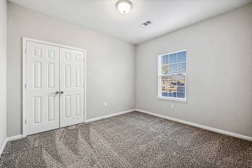 A room with a carpeted floor, a white door, and a window with blinds.