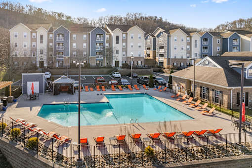 A large swimming pool surrounded by orange chairs in front of apartment buildings at Evergreen at the Bluffs apartments in Knoxville, TN..