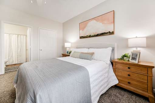A bedroom with a large bed, a nightstand, and a painting on the wall.