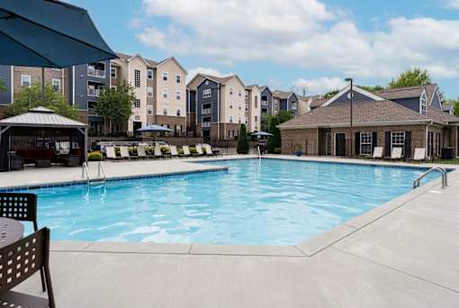 A pool area with a bench and a gazebo in front of apartment buildings.
