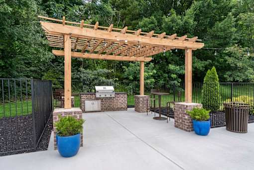 A wooden pergola is over a patio with a table and chairs.
