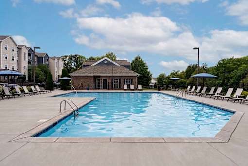A large outdoor swimming pool with lounge chairs and a building in the background.