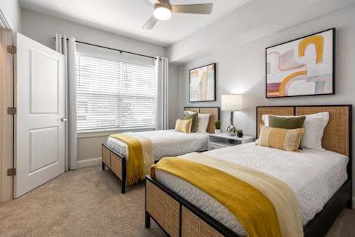 Two beds with yellow blankets in a room with a ceiling fan.