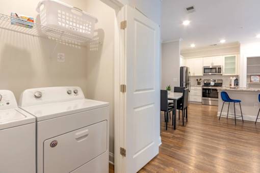 A laundry room with a washer and dryer and a kitchen area with a table and chairs.