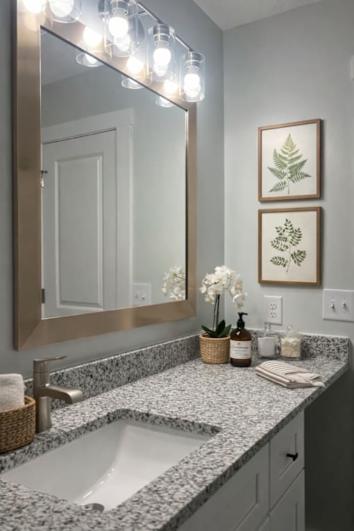 A bathroom with a marble countertop and a large mirror above the sink.