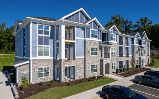 A modern apartment complex with multiple buildings and cars parked in the driveway.