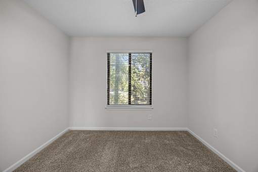 A bedroom with a carpeted floor and a window with blinds.